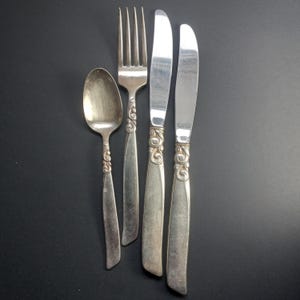 Puede incluir: Un juego de cuatro piezas de cubiertos plateados, que incluyen un tenedor, un cuchillo, una cuchara y otro cuchillo. Los mangos tienen un diseño adornado.