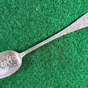 Puede incluir: Una cuchara de plata con un diseño ornamentado y la palabra "EDOWNA" grabada en el cuenco.