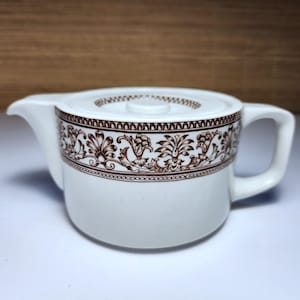 May include: White ceramic teapot with a brown floral pattern around the body and on the lid. The teapot has a spout, a handle, and a lid with a small knob. The design is a classic, vintage style.