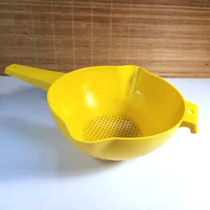 Puede incluir: Un colador de plástico amarillo brillante con un mango largo y una base perforada. El colador tiene forma de cuenco redondeado con un pico vertedor y un pequeño asa lateral. Diseñado para colar líquidos.