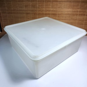 Może przedstawiać: Kwadratowy, półprzezroczysty biały plastikowy pojemnik do przechowywania z dopasowaną pokrywką. Pojemnik ma płaską górną powierzchnię i proste pionowe ścianki, co zapewnia prosty i funkcjonalny design do organizowania różnych przedmiotów domowych.