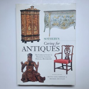 Peut inclure: La couverture du livre "Sotheby's Caring for Antiques" présente des meubles anciens et une statue. Le sous-titre du livre est "Le guide complet de la manipulation, du nettoyage, de l'exposition et de la restauration".