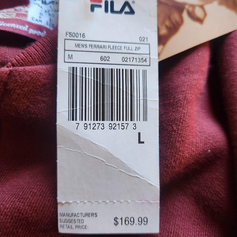 May include: A close-up of a maroon Fila Ferrari fleece full zip sweatshirt. The tag shows the size is large. The tag also shows the Fila logo and the text "MEN'S FERRARI FLEECE FULL ZIP".