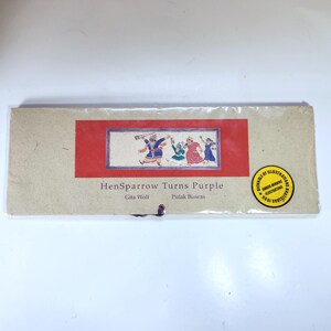 Puede incluir: Un paquete rectangular con el título "HenSparrow Turns Purple". El paquete tiene un rectángulo rojo con una ilustración de personas bailando. Una pegatina dorada con texto está en el lado derecho.