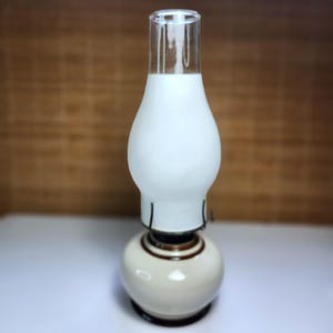 Peut inclure: Une lampe à huile vintage avec un abat-jour en verre dépoli blanc et une cheminée en verre transparent. La base est de couleur crème avec des accents marron. La lampe est conçue pour être posée sur une surface plane.