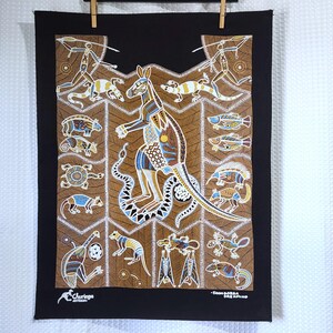 May include: A black fabric wall hanging featuring a central kangaroo surrounded by various Australian animals and figures in a dot art style. The brown background has intricate patterns, and the text reads Churinga Australia and Koon-Garra Dreaming.