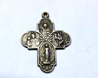 Może przedstawiać: Srebrny wisiorek z krzyżem religijnym z szczegółowymi grawerunkami. Krzyż przedstawia wizerunki postaci i symboli religijnych, w tym centralne przedstawienie stojącej postaci i otaczających ilustracji. Wisiorek ma pętlę na łańcuszek.
