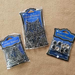 May include: Three packages of Global Nomad metal pendants and connectors. The packages are sealed in clear plastic and feature a blue and white label. The metal pieces are silver-toned and include ornate pendants and connectors.