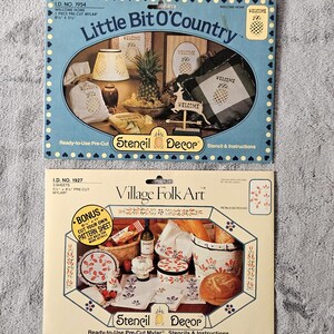 May include: Two vintage stencil decor kits. The top kit, "Little Bit O'Country," features a pineapple theme. The bottom kit, "Village Folk Art," showcases floral and food designs. Both kits include pre-cut mylar stencils and instructions.