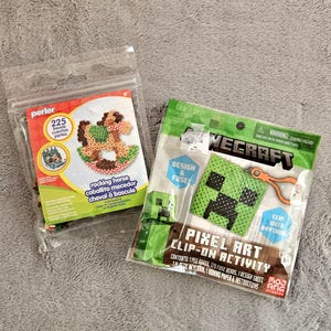 May include: Two Perler and Minecraft fuse bead activity kits in clear plastic packaging. The Perler kit features a rocking horse design with 225 beads. The Minecraft kit includes a green Creeper pixel art design with a clip-on attachment.