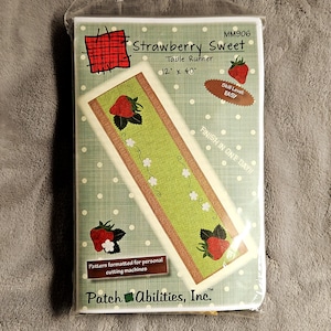 May include: A Strawberry Sweet table runner craft pattern package measuring 12 inches by 40 inches. The packaging features a light green background with white polka dots, strawberry illustrations, and the text Patch Abilities, Inc. MM906.