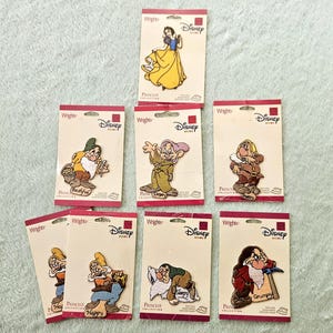 May include: A collection of Disney character patches, including Snow White and the seven dwarfs. Each patch is on a cardboard backing with the Disney and Wrights logos. The patches feature vibrant colors and detailed character designs.