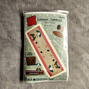May include: A sewing pattern package titled Summer Yummies for a 12 inch by 40 inch table runner. The packaging features a light green background with white polka dots, illustrations of ice cream treats, and a finished table runner design.