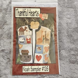 May include: A craft pattern titled "Thankful Hearts" featuring a vest design with various appliqued images, including a camel, sheep, and giraffes. The pattern is labeled "Noah Sampler #126" and is packaged in a clear plastic bag.