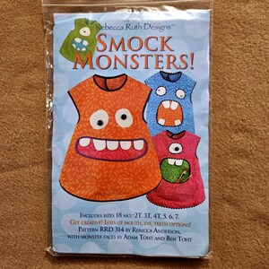 May include: A package for a sewing pattern titled "Smock Monsters!" features illustrations of monster-themed smocks in orange, blue, and pink. The text includes sizes from 18 months to size 7, and mentions mouth, eye, and teeth options.