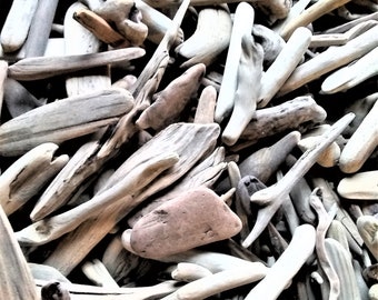 May include: A collection of assorted driftwood pieces in various shapes and sizes, featuring weathered textures and natural shades of gray, tan, and brown. The assortment includes smooth, rounded fragments and elongated, branch-like wooden elements.