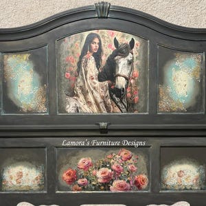 May include: A black painted headboard with a decorative arched top and a floral design. The headboard features a central panel with a woman riding a white horse, surrounded by roses. The text "Lamora's Furniture Designs" is printed on the headboard.
