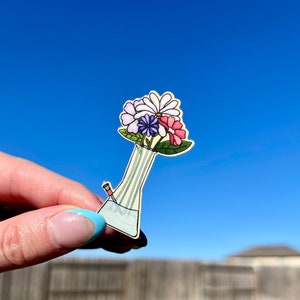 May include: A sticker of a glass bong with a bouquet of colorful flowers in the top. The flowers are pink, purple, white, and yellow.