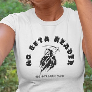 May include: White t-shirt featuring a black graphic of a grim reaper holding a scythe. The graphic is surrounded by the text "No Beta Reader" in a black, bubble-like font. The text "We Die Like Men" is printed below the graphic.