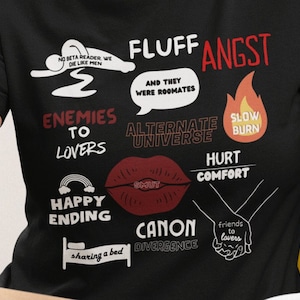 May include: Black t-shirt with white text and illustrations. The text includes "Fluff Angst", "Enemies to Lovers", "Happy Ending", "Canon Divergence", "Alternate Universe", "Slow Burn", "Hurt Comfort", "Friends to Lovers", "And They Were Roommates", "Sharing a Bed", "No Beta Reader, We Die Like Men", and "Smut".