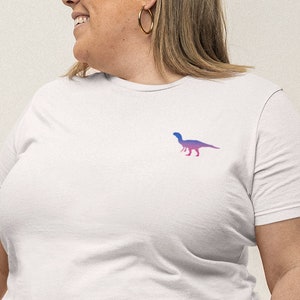 Könnte beinhalten: Weißes T-Shirt mit einer pinkfarbenen und blauen Dinosauriersilhouette auf der Vorderseite.