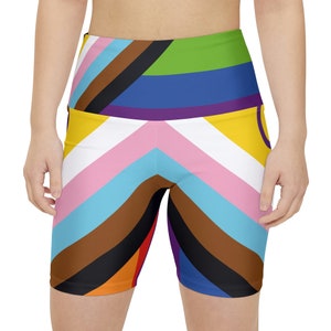 Può includere: Pantaloncini da ciclista a vita alta con un design vibrante e colorato. I pantaloncini presentano un motivo a strisce in vari colori, tra cui rosa, blu, marrone, nero, giallo, verde e viola. Il design è una rappresentazione della bandiera del Pride.