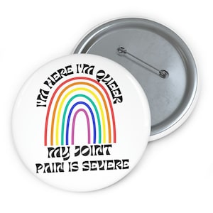 Può includere: Un bottone bianco con un arcobaleno e il testo "I'm here I'm queer my joint pain is severe".