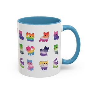 May include: White ceramic mug with a blue interior and handle. The mug is decorated with colorful cartoon cat illustrations. The cats have rainbow, pink, orange, purple, and green color schemes. The mug is a standard 11 oz size.