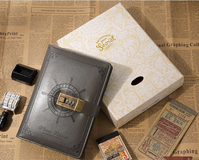 May include: A gray leather-bound journal with a combination lock and a compass design. The journal is closed and has the text "permanent your secret" on the box it is in.
