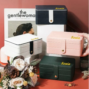 May include: Four jewellery boxes with three tiers each. The boxes are in black, white, pink, and green. Each box has a gold clasp and a gold inscription that reads "Sonia".