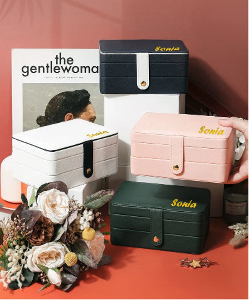 May include: Four jewellery boxes with three tiers each. The boxes are in black, white, pink, and green. Each box has a gold clasp and a gold inscription that reads "Sonia".