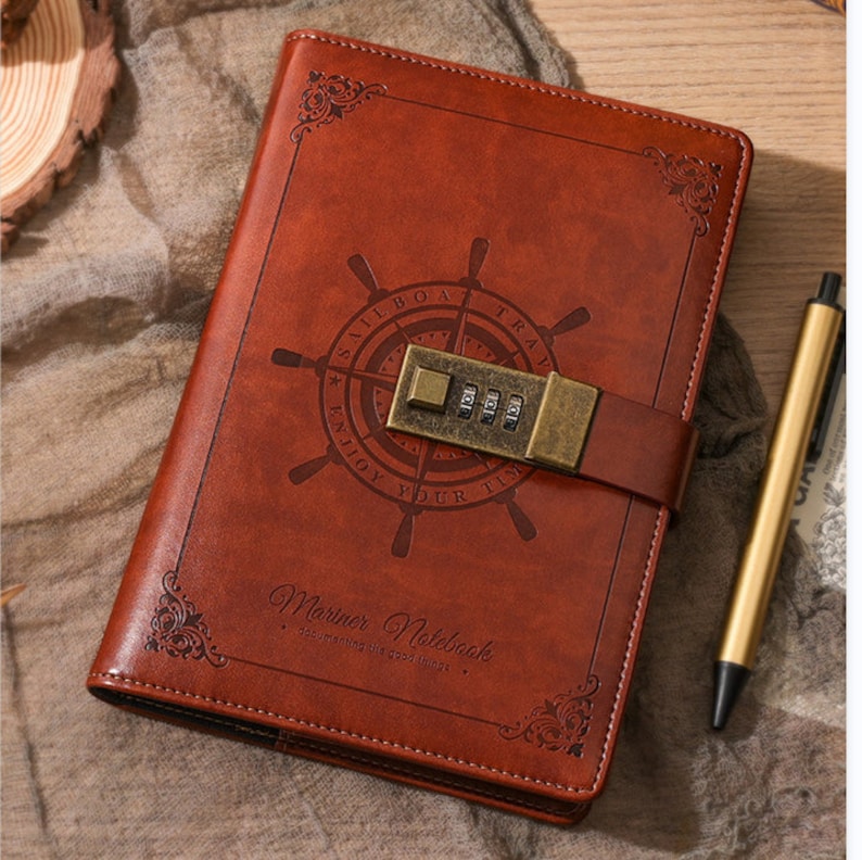 May include: Brown leather journal with a brass lock and a compass design. The journal has the text "Sailboat Travel Enjoy Your Time" and "Mariner Notebook - Documenting the good things" on the front cover.