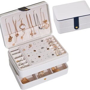May include: White jewellery box with two layers. The top layer has compartments for necklaces, earrings, and rings. The bottom layer has compartments for rings and other small jewellery. The box has a blue and white design.