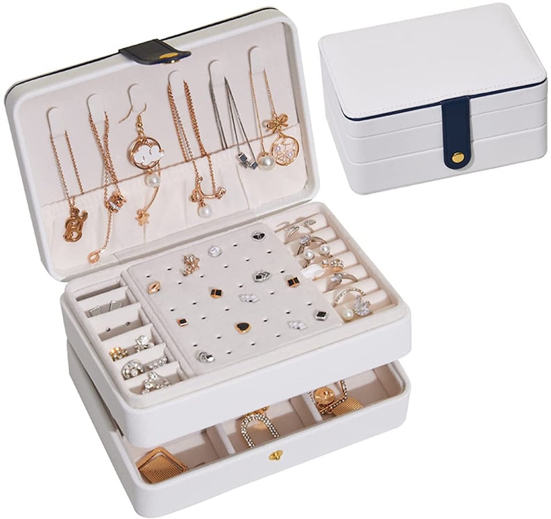 May include: White jewellery box with two layers. The top layer has compartments for necklaces, earrings, and rings. The bottom layer has compartments for rings and other small jewellery. The box has a blue and white design.