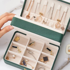 May include: A green jewellery box with a hinged lid. The top compartment has slots for necklaces and the bottom compartment has compartments for earrings and rings.