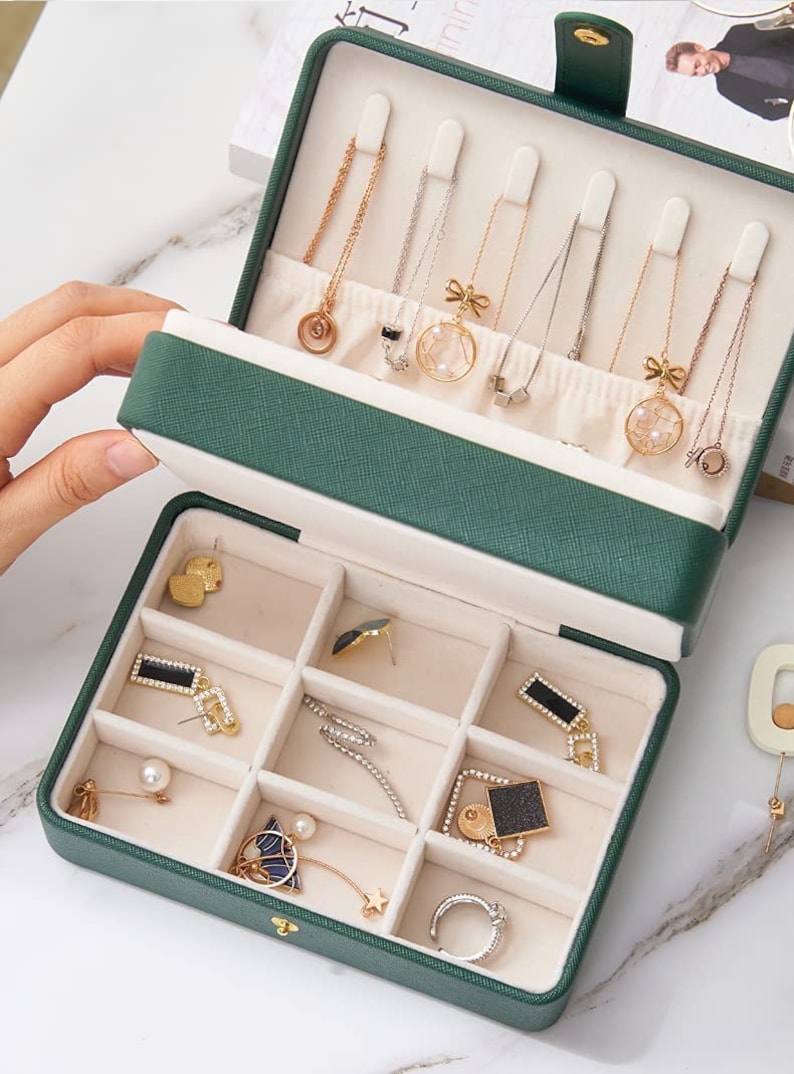 May include: A green jewellery box with a hinged lid. The top compartment has slots for necklaces and the bottom compartment has compartments for earrings and rings.