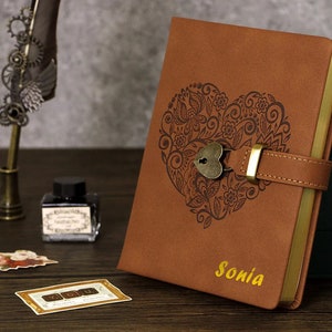 Peut inclure: Journal en cuir marron avec une serrure et une clé dorées, un motif de cœur décoratif et le nom "Sonia" en relief en lettres dorées.
