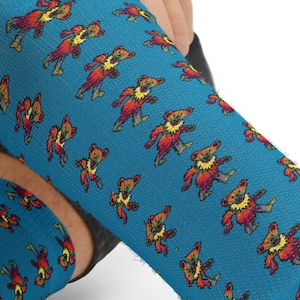May include: A pair of blue socks with a repeating pattern of dancing bears in red, yellow, and brown. The socks are pulled up on a person's leg, showcasing the design and fit. The socks are made of a soft, comfortable material.