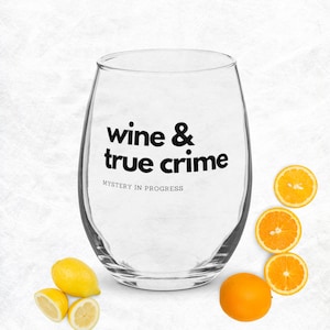 May include: A stemless wine glass with the words "wine & true crime" printed in black. The phrase "Mystery in Progress" is printed below. The glass is surrounded by sliced oranges and lemons.