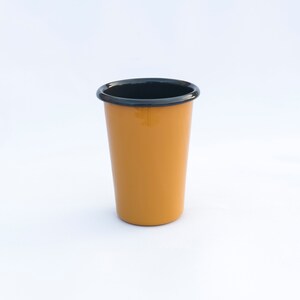 Yellow enamel tumbler cup with anthracite rim, placed on a white surface, with a plain background.