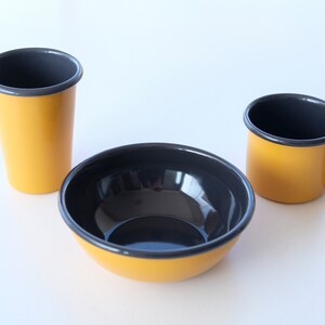 A sophisticated yellow enamelware set with contrasting anthracite rims, perfect for stylish dining, comprising a bowl, mug, and tumbler.