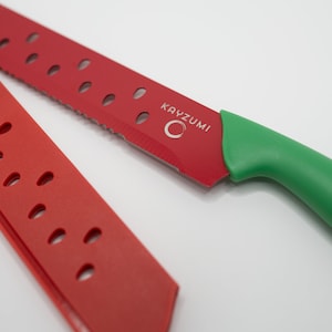 May include: A red and green watermelon knife with a serrated blade and a green handle. The knife has the brand name "KAYZUMI" printed on the blade.