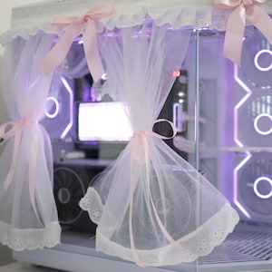 Peut inclure: Un boîtier d'ordinateur blanc avec un panneau latéral en verre, orné de dentelle blanche et de rubans roses. Le boîtier est doté d'un rideau en tulle et l'intérieur est éclairé d'une lumière violette. Un mélange unique de technologie et d'esthétique délicate.