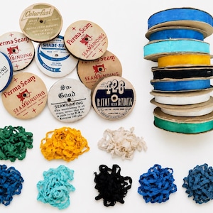 May include: A collection of vintage rayon seam binding ribbon on round cardboard spools with printed labels including Perma-Seam and 426, alongside loose piles of colorful ribbon in green, yellow, white, blue, turquoise, and black hues.