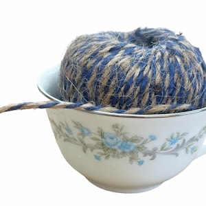 May include: A ball of blue and brown twine is sitting in a white teacup with a floral pattern. The twine is spilling out of the cup.