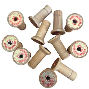 May include: A collection of ten wooden spools with red and white labels. The labels have text that reads "Holland Thread Co. Inc." and "Pure de Machine Silk".