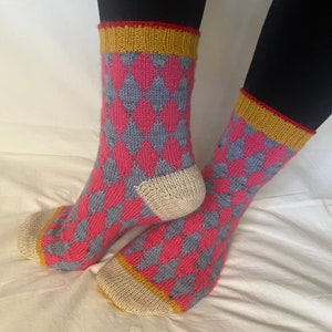 May include: A pair of knitted socks with a diamond pattern in pink and blue. The socks have a yellow band at the top.