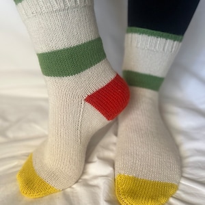 May include: A pair of white socks with green and red stripes and yellow toes. The socks are knitted and have a casual style.