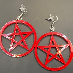 May include: A pair of red acrylic earrings with a pentagram design. The earrings are silver and have a hook closure.