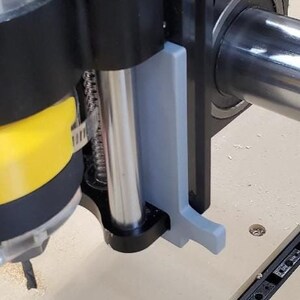 May include: Close-up of a black and silver router bit holder with a gray plastic guard. The holder is attached to a metal base.